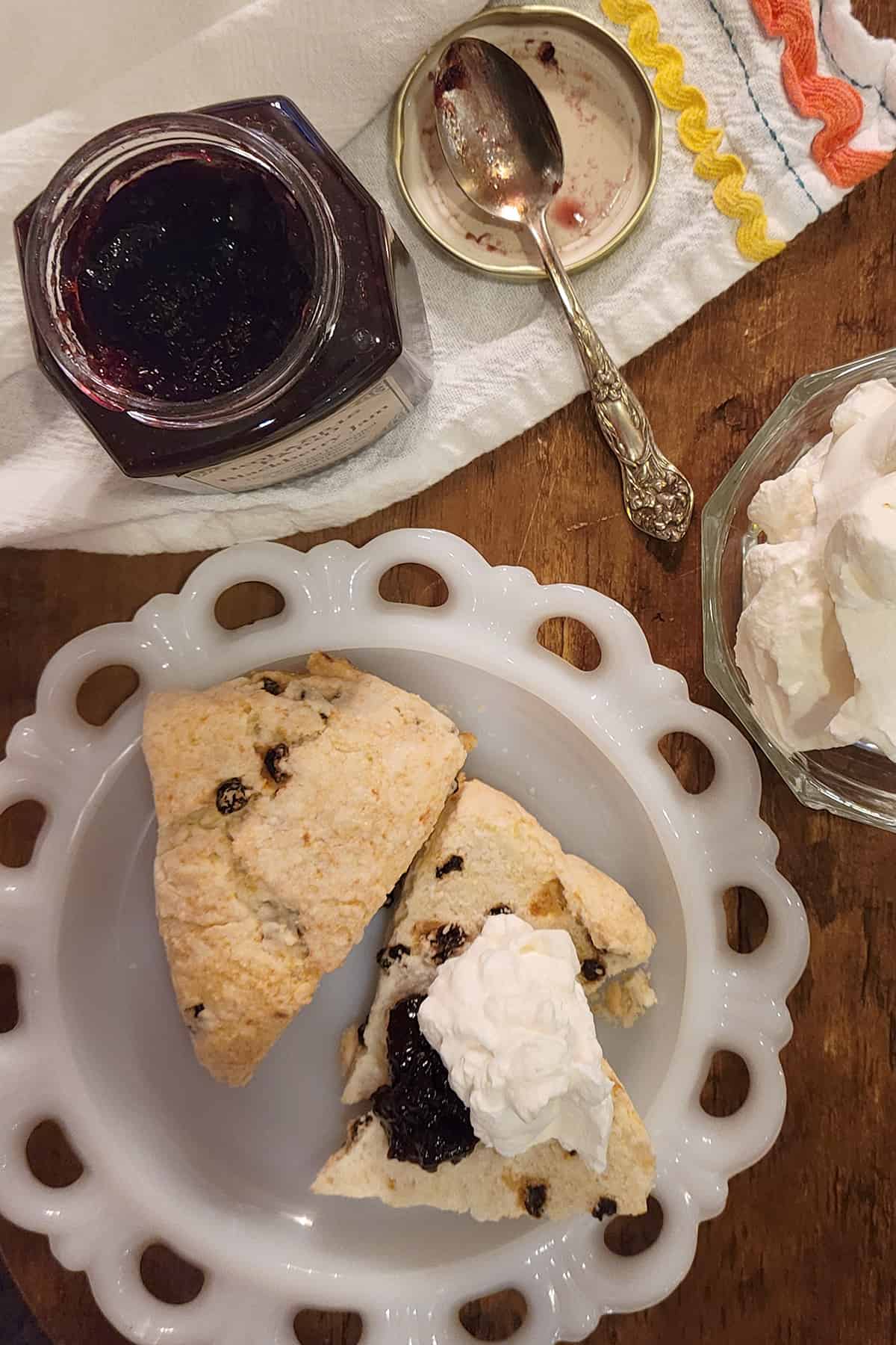 Two scones spread with jam and cream on a white plate.