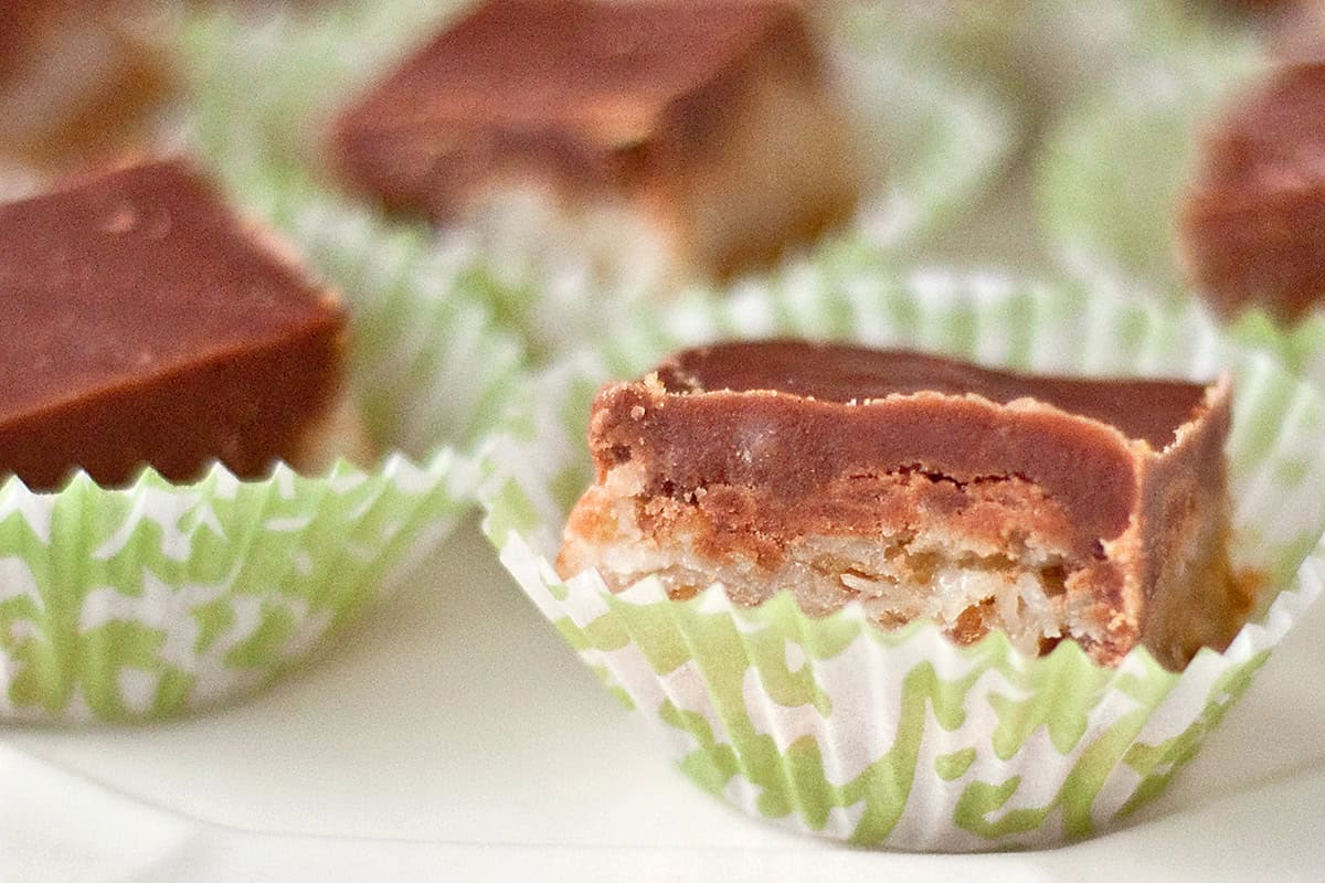 A close-up of chocolate-topped dessert squares in green and white paper cups, one with a bite taken out.