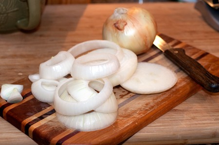 Thickly sliced rings of raw onion on a cutting board