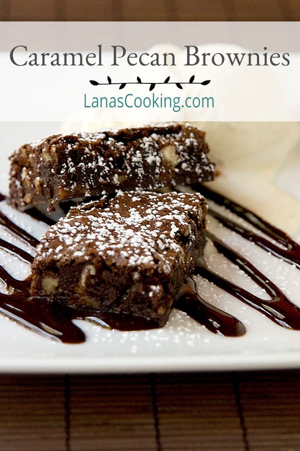 Caramel Pecan Brownies drizzled with chocolate syrup and topped with powdered sugar.