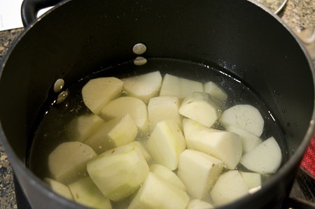 Potatoes cooking in water in a large pot.