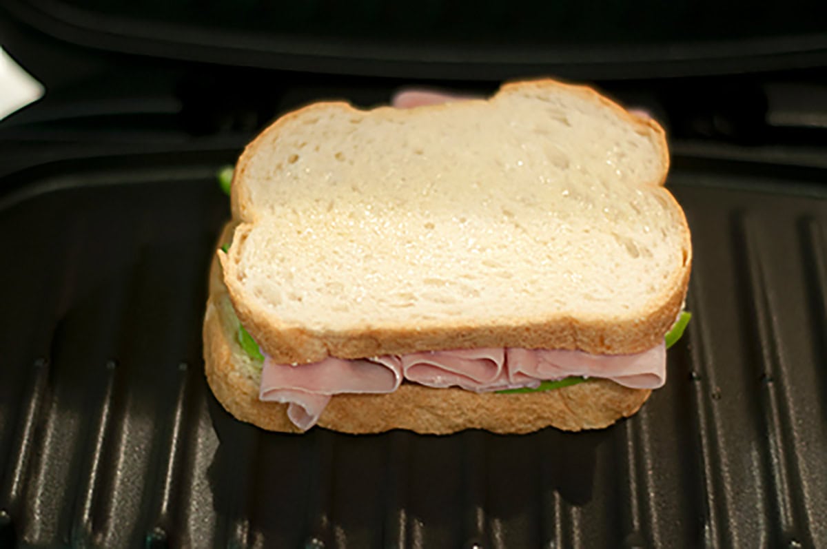 Uncooked ham apple brie panini placed on a panini press grill.