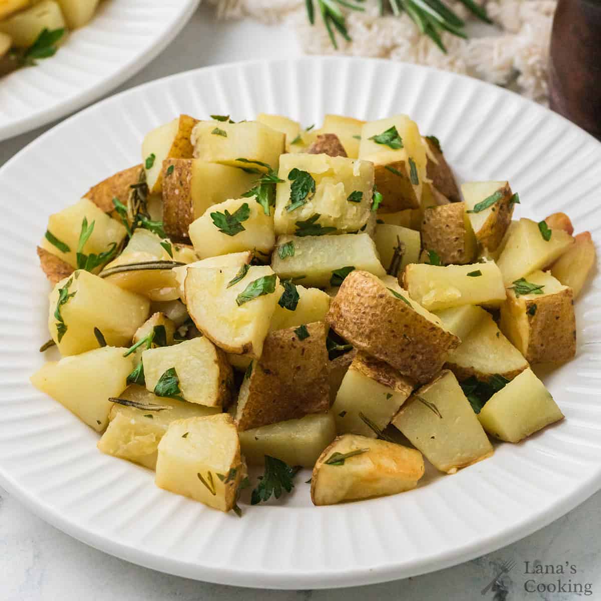 A white plate filled with roasted potato cubes garnished with chopped parsley and rosemary.