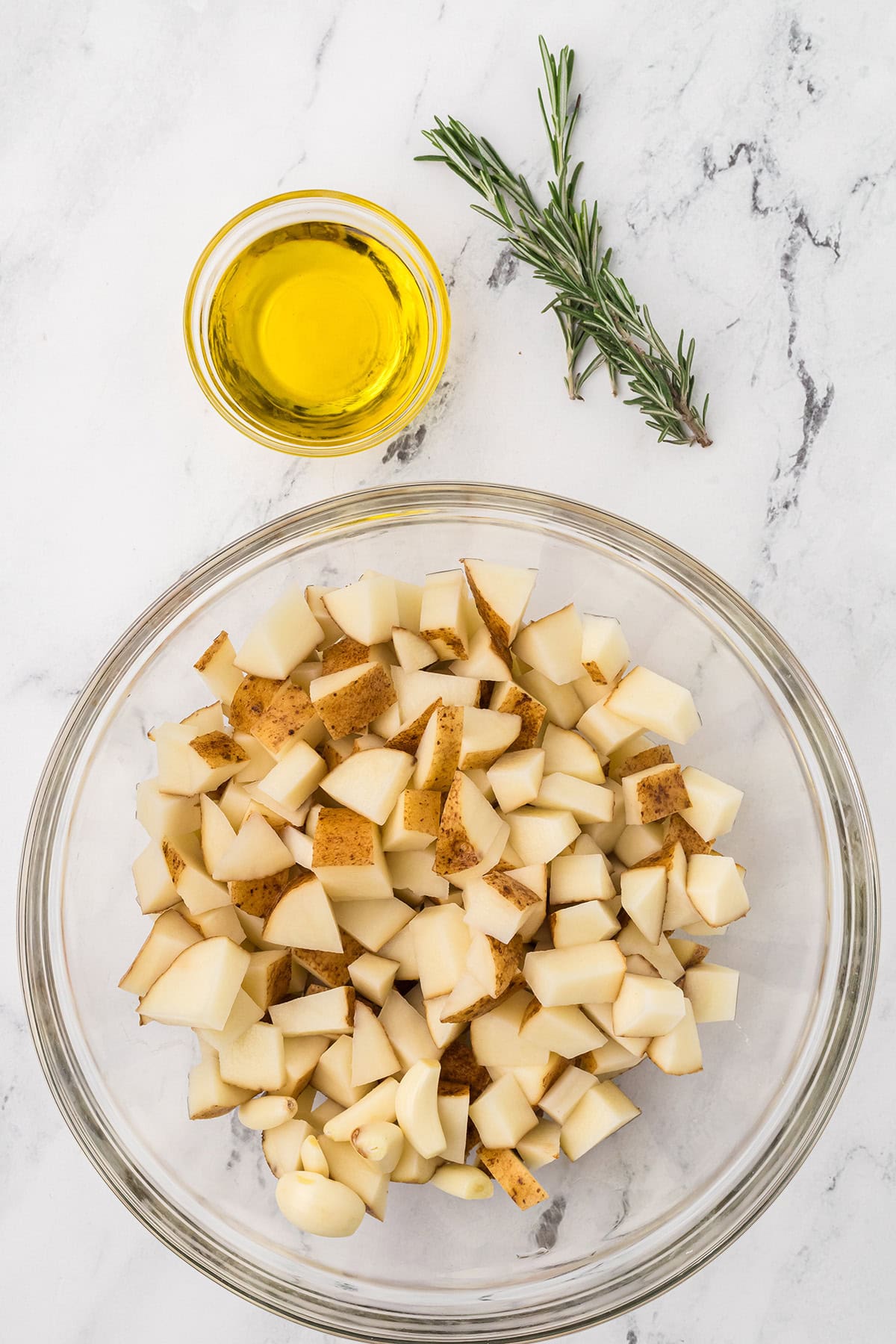 Cubed potatoes in a glass bowl sitting on a marble surface.