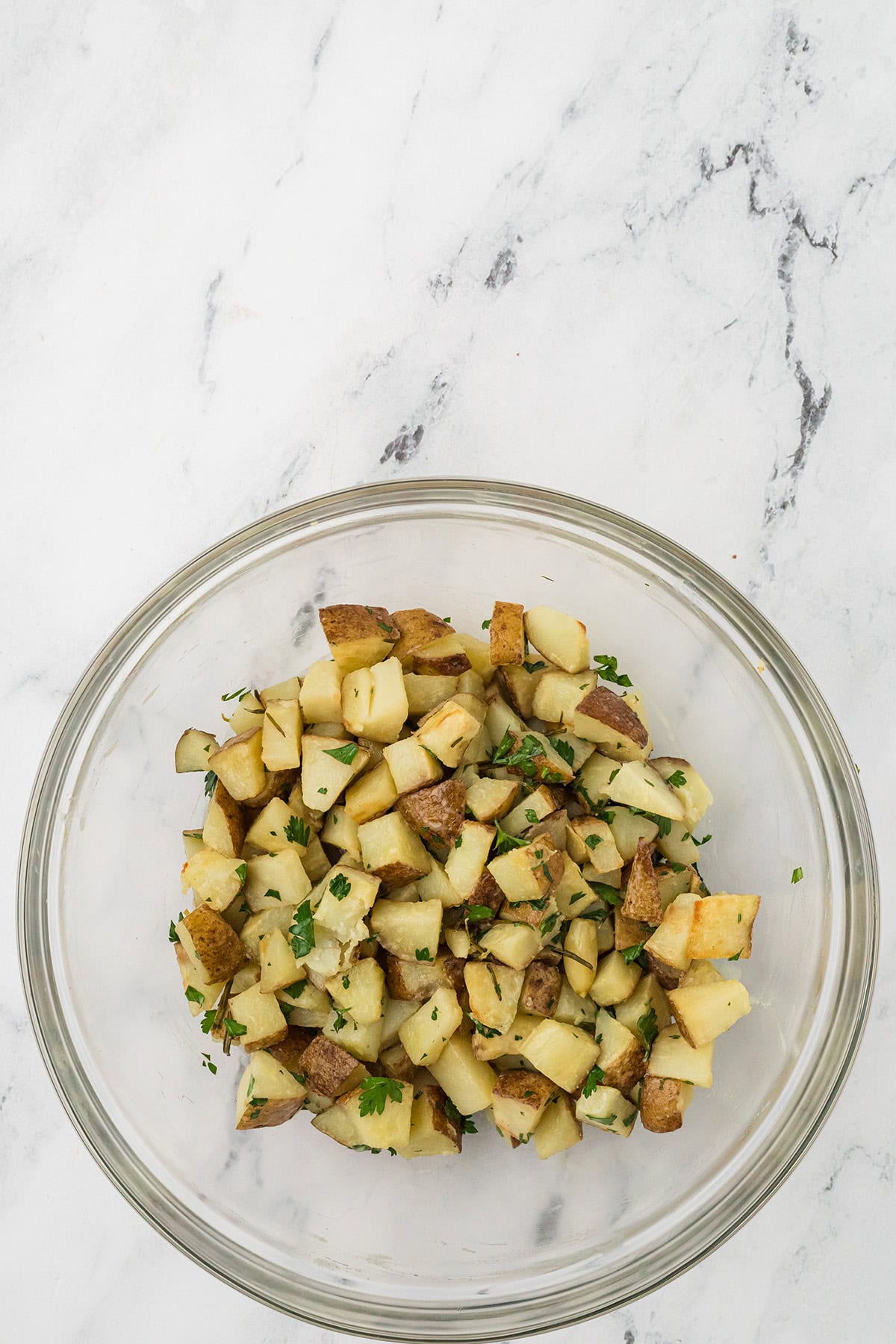 Roasted potatoes combined with dressing in a bowl.