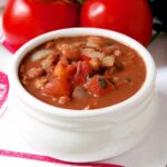 Cowgirl beans in a white serving bowl with fresh tomatoes in the background.