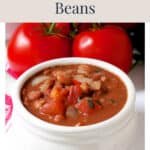 A bowl of tomato-based cowgirl beans with two whole tomatoes in the background.