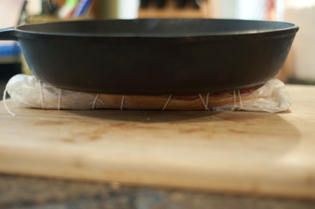Wrapped sandwich being pressed under a cast iron skillet.
