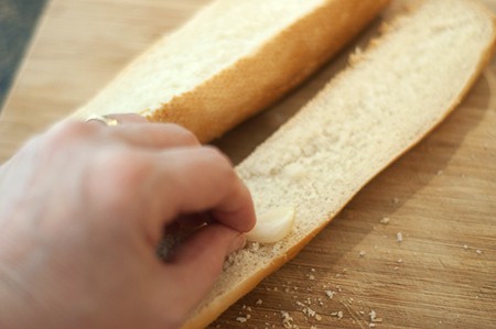 Cut sides of baguette being rubbed with a garlic clove.