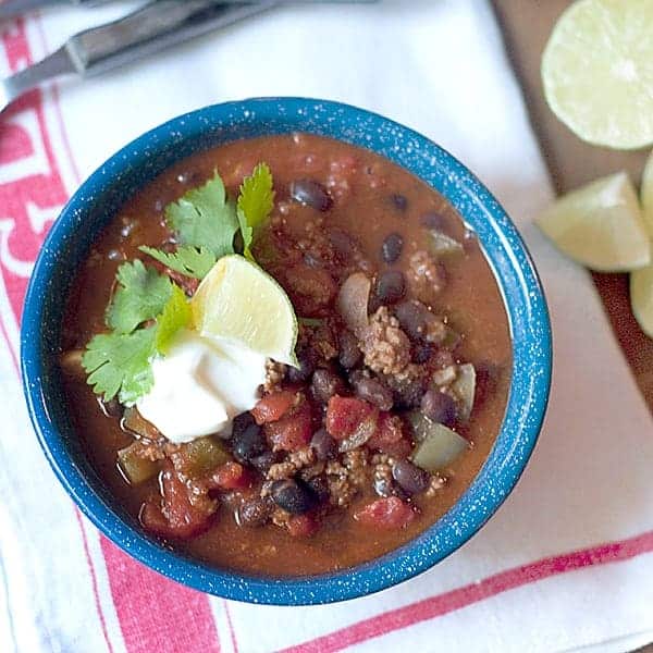 Black Bean Chili - a hearty, beefy chili rich with tomatoes, black beans, and spices. Top with sour cream and fresh cilantro. Pass lime wedges. https://www.lanascooking.com/black-bean-chili/
