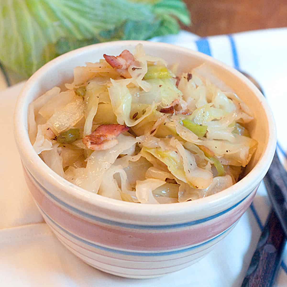 A bowl of cooked cabbage with bacon pieces, served on a striped cloth.
