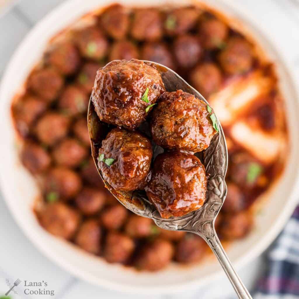 A serving spoon holding sweet and sour meatballs.