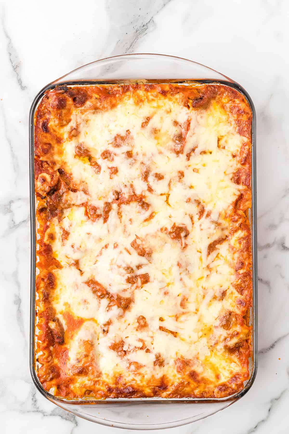 A baked lasagna in a glass dish topped with melted cheese on a marble surface.