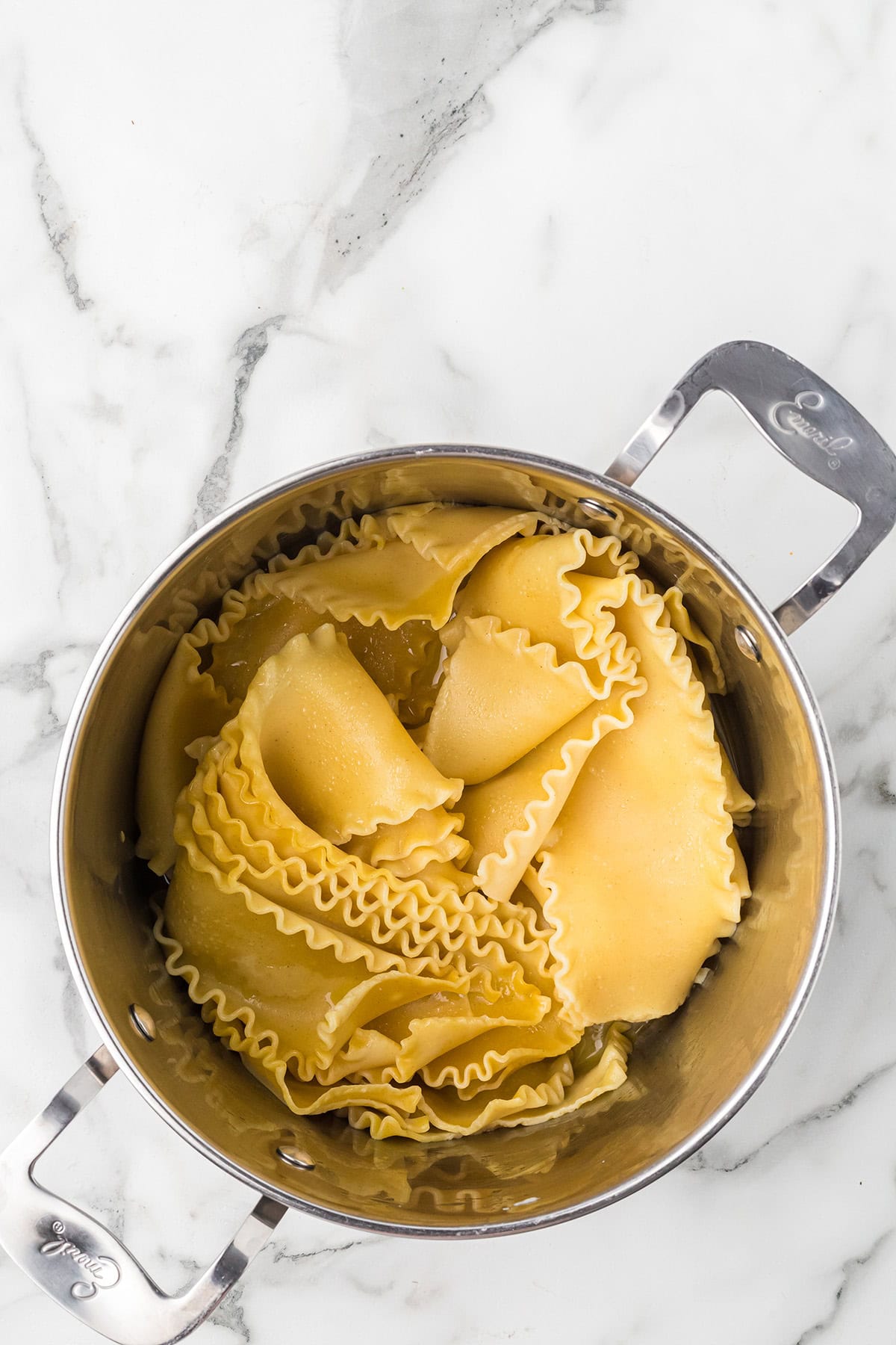 Cooked lasagna noodles in a stainless steel pot on a white marble surface.