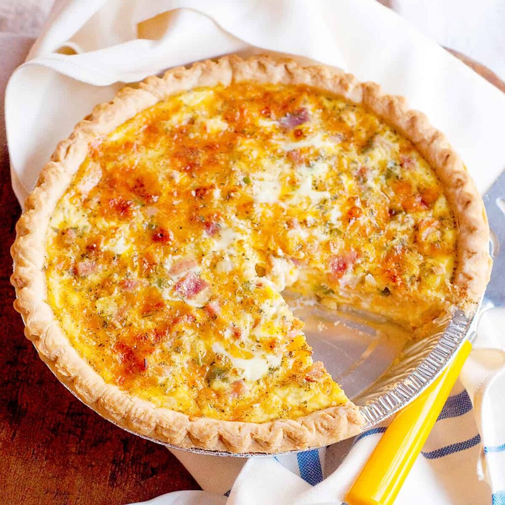 Ham and Cheese Quiche on a serving board with a slice on a plate.