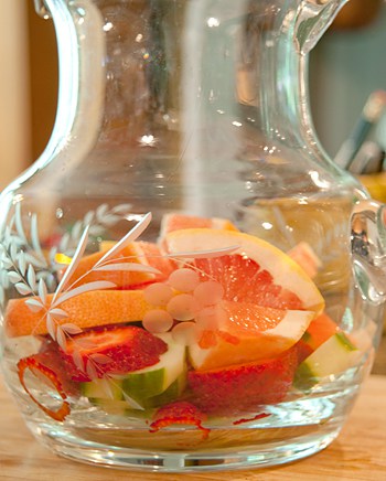 Fresh fruits layered in a glass pitcher.