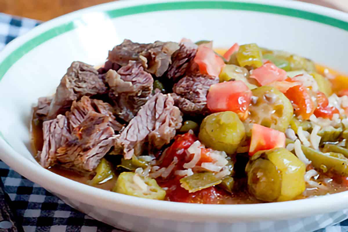 A bowl of soup with okra, tomatoes, and shredded cheese on top.
