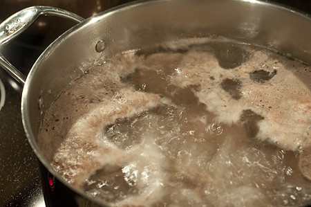 Skim the "scum" from the soup Beef short ribs cooking in a soup pot.