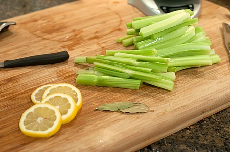 A cutting board with prepared celery sticks and lemon slices.