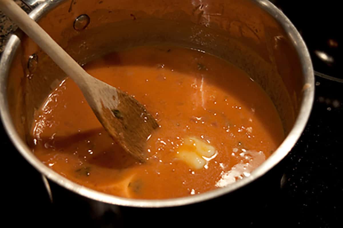 Stirring butter into the sauce in a pan.