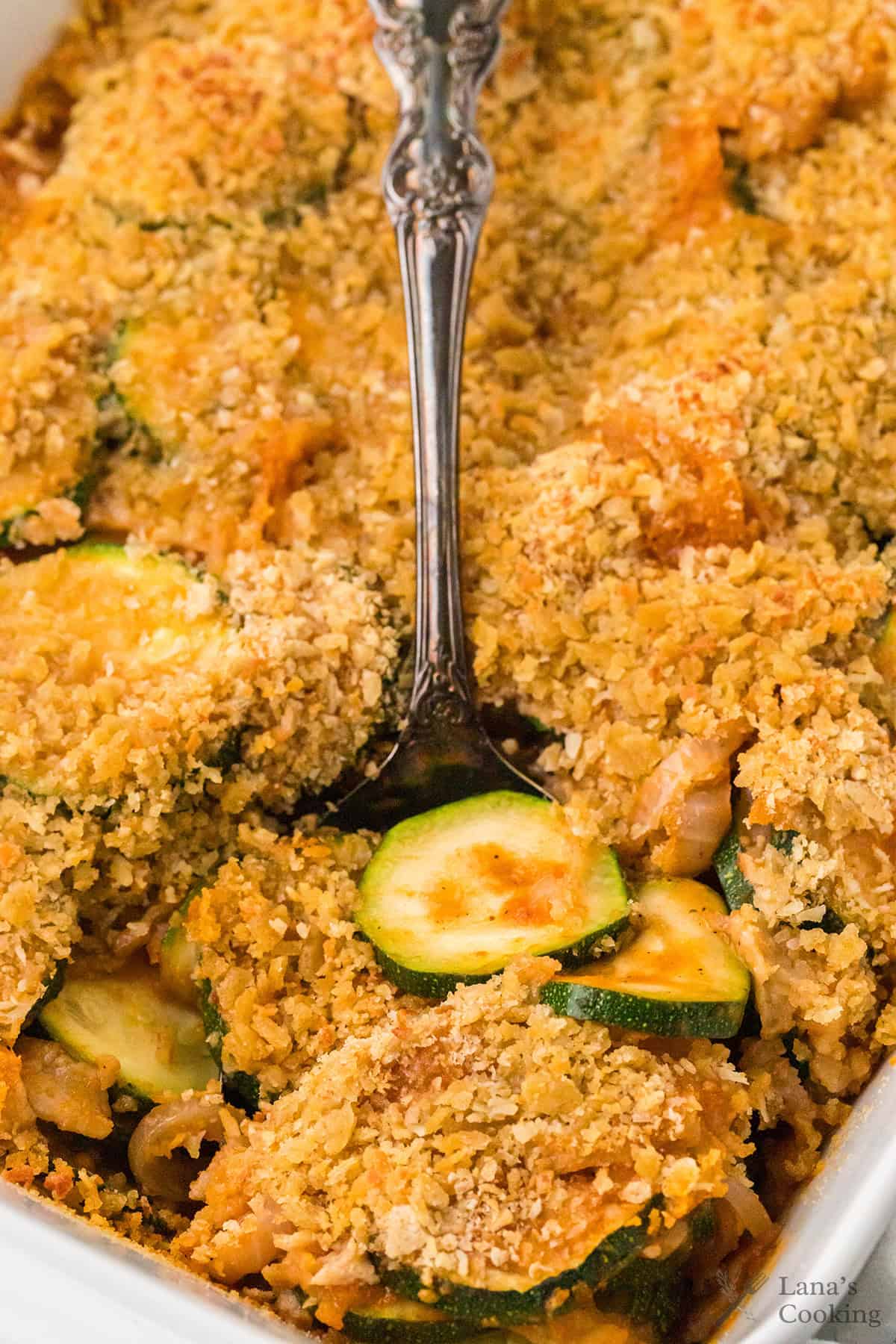 A spoon scooping zucchini casserole topped with a golden, crispy cracker crust.