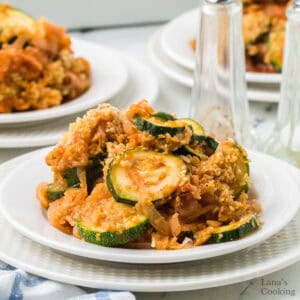 A plate of baked zucchini casserole with breadcrumbs, served on a white dish with more plates in the background.