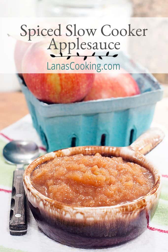 Bowl of applesauce with a basket of fresh apples on a kitchen towel. Text overlay for pinning.