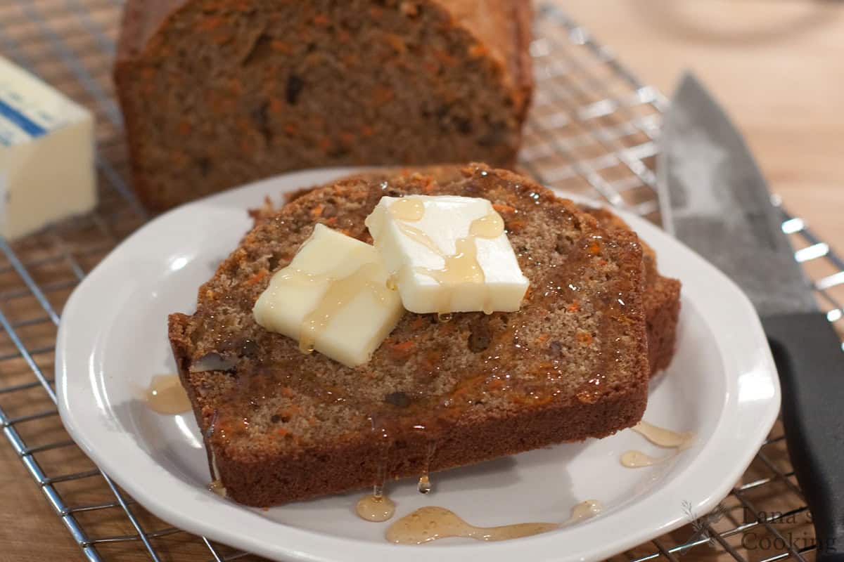 A slice of carrot pecan quick bread topped with butter and honey on a white plate.