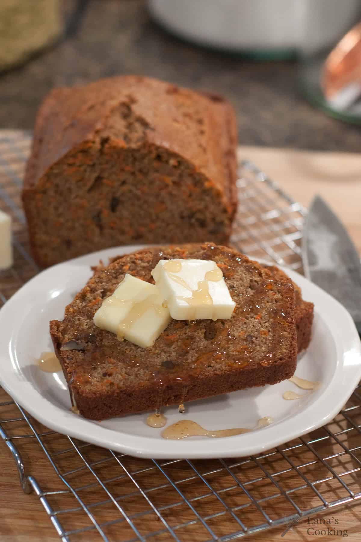 A slice of carrot pecan bread topped with butter and honey, with a loaf in the background.