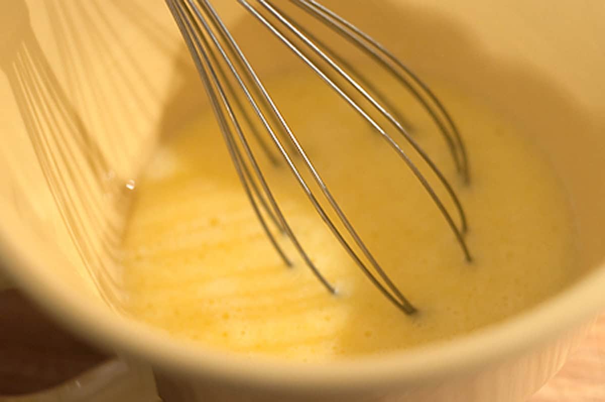 A wire whisk mixing eggs in a bowl.