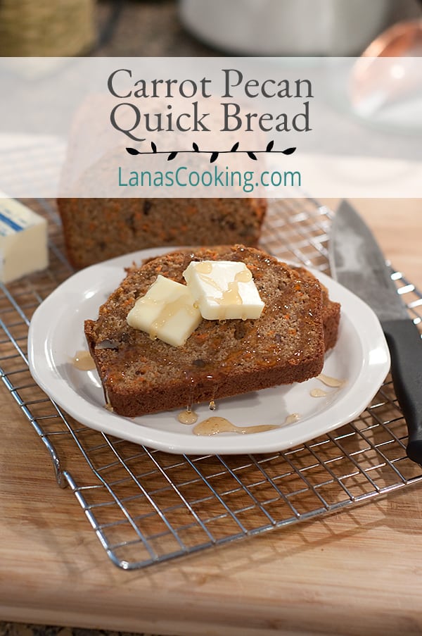 A slice of carrot pecan quick bread on a plate topped with butter and honey.