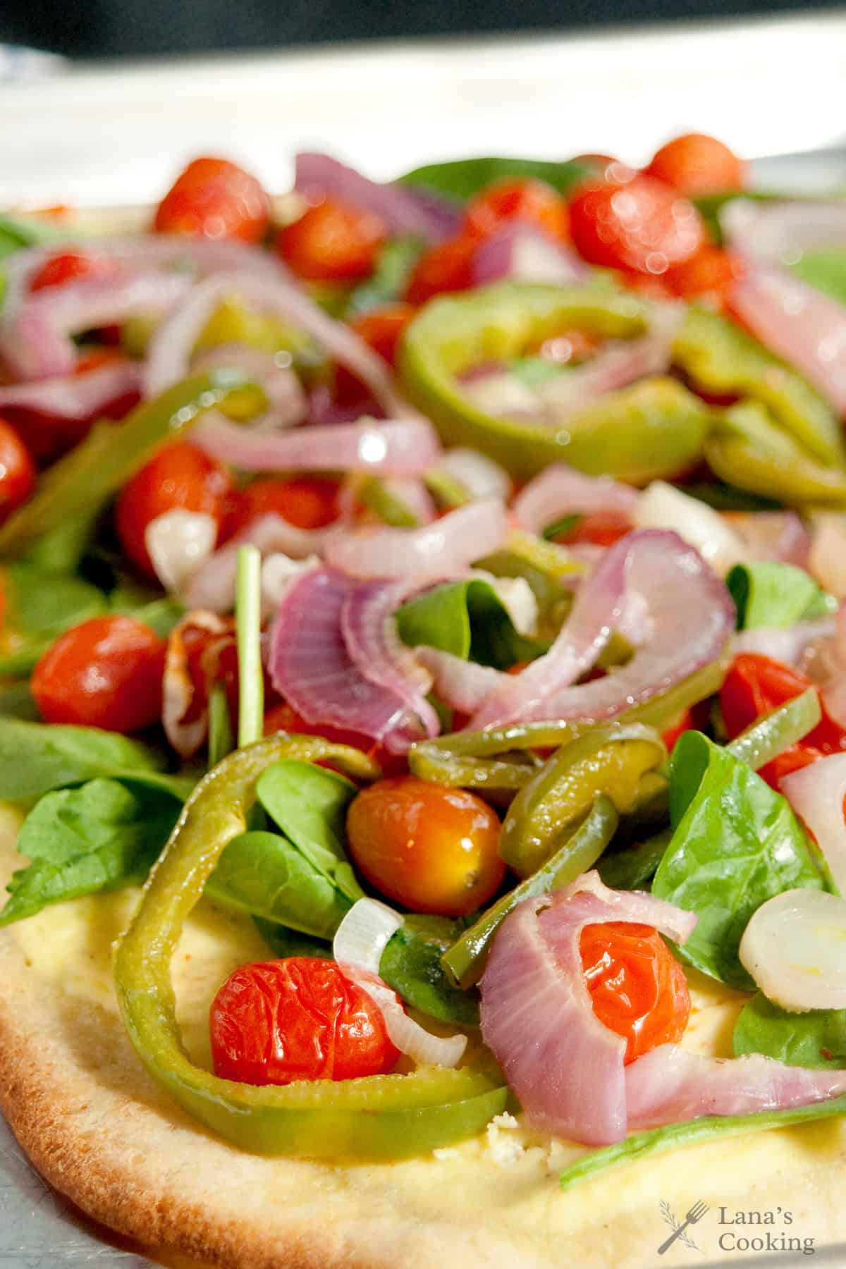 Close-up of a vegetable pizza topped with spinach, cherry tomatoes, green bell peppers, and red onions on a thin crust.