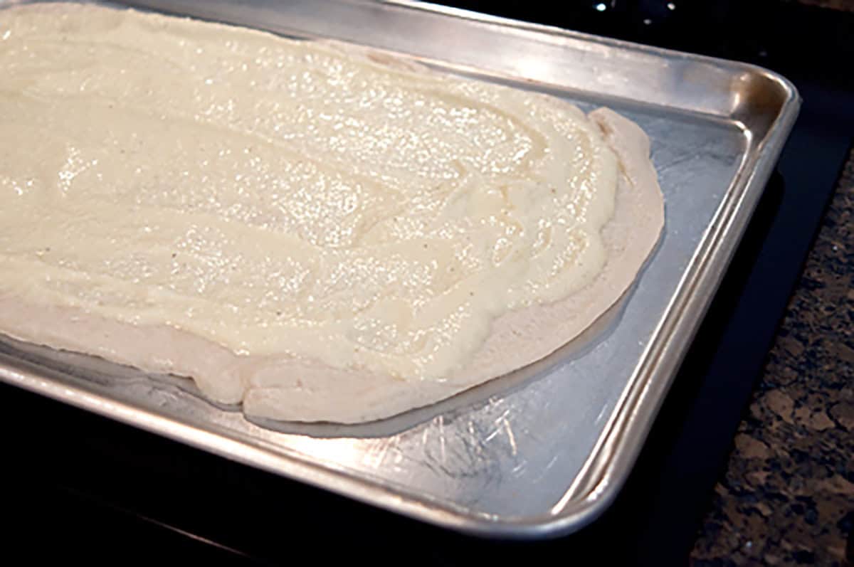 Unbaked pizza dough topped with a ricotta mixture on a metal baking sheet.