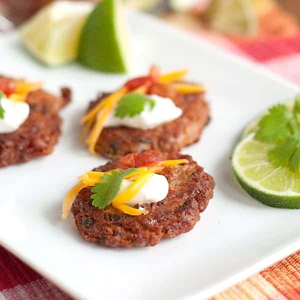 Pinto bean cakes on a white plate with lime and cilantro on the side.