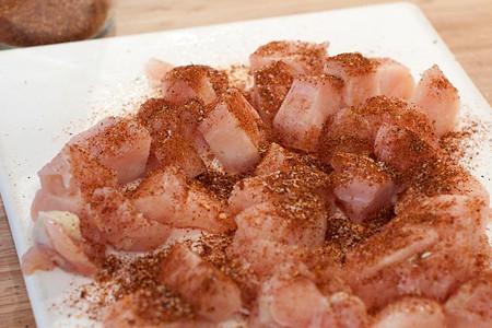 Seasoned chicken breast pieces on a board.