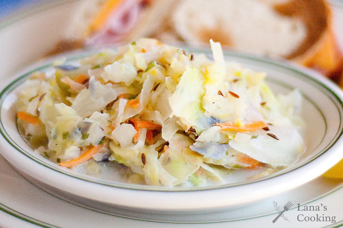 A plate of creamy hot cabbage slaw with shredded cabbage and carrots, garnished with caraway seeds.