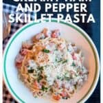 Bowl of creamy ham and pepper pasta with grated cheese on top, placed on a checkered cloth with utensils.