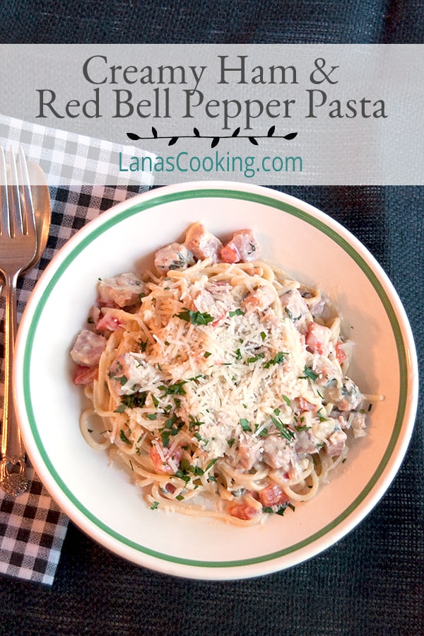 A serving of creamy ham and red bell pepper pasta in a bowl with a fork alongside.