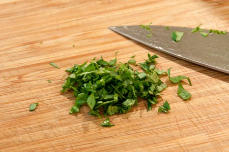 Minced fresh basil with a knife on a cutting board.