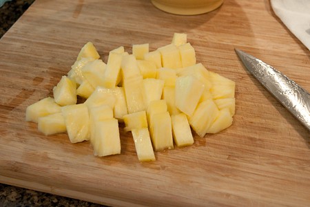 Fresh pineapple cut into bite-sized pieces with a knife on a cutting board.