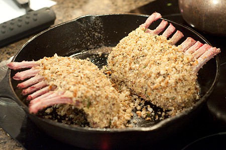 Crumb coated racks of lamb in a large heavy frying pan.