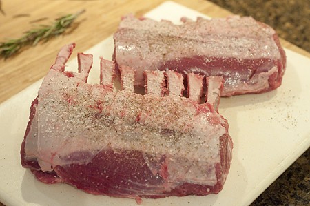 Two racks of lamb coated with salt and pepper.