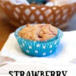 A strawberry lemon muffin sitting on a napkin with a basket of muffins in the background.