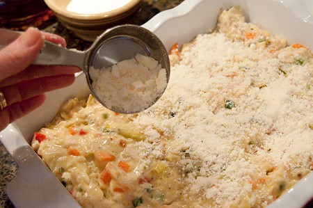 Casserole mixture in a baking dish being topped with Parmesan.
