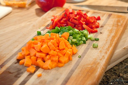 Carrot, red pepper, and onions prepped on a cutting board.