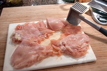 Prepping chicken with a meat mallet on a cutting board.