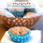 A strawberry lemon muffin sitting on a napkin with a basket of muffins in the background.