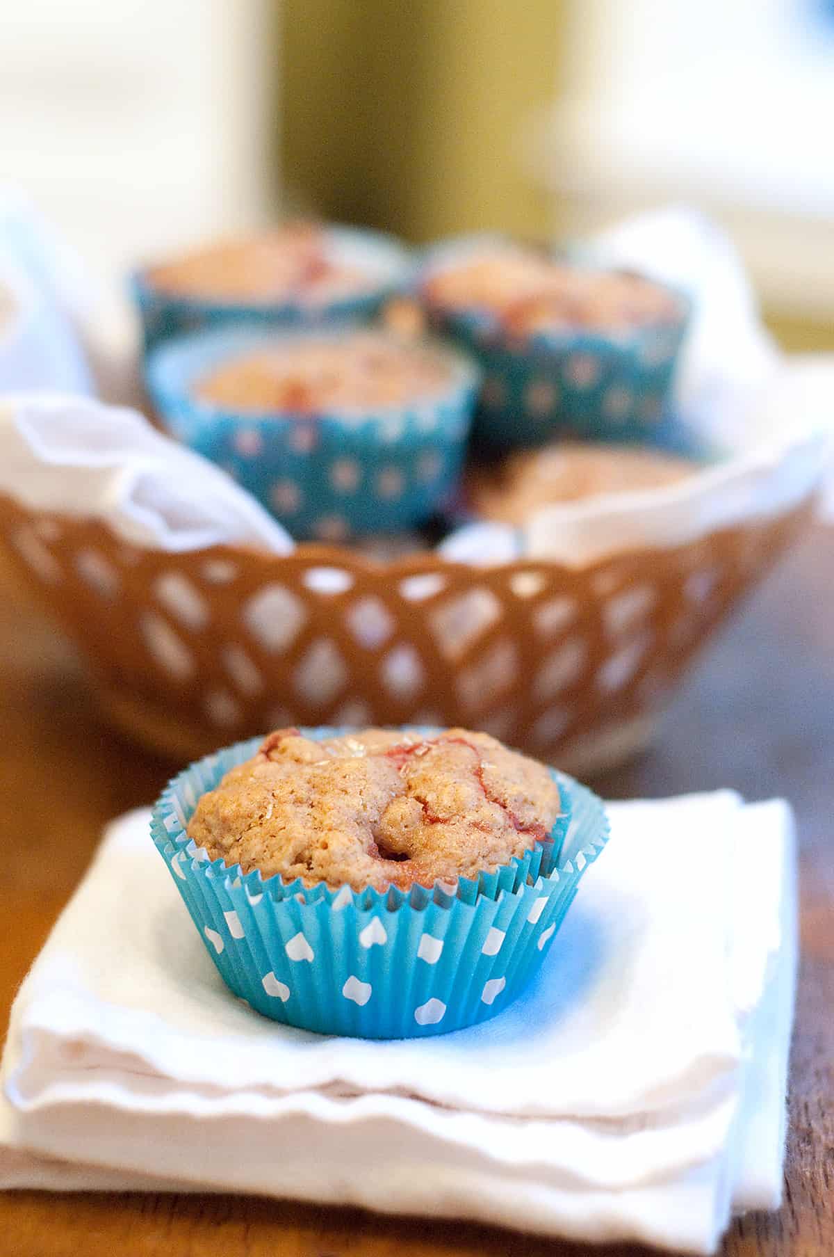 A strawberry lemon muffin sitting on a napkin with a basket of muffins in the background.