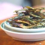 Crispy oven baked okra chips piled high in a white and green bowl.