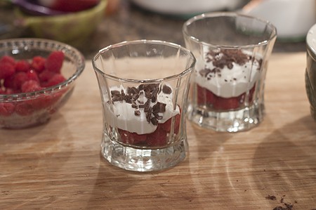 Layering raspberries, whipped cream, and chocolate in glasses.